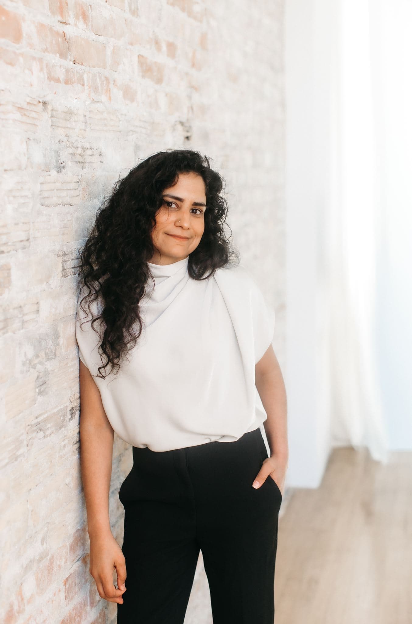 Alisha Esmail, AI operations consultant, leaning against a brick wall in a bright studio